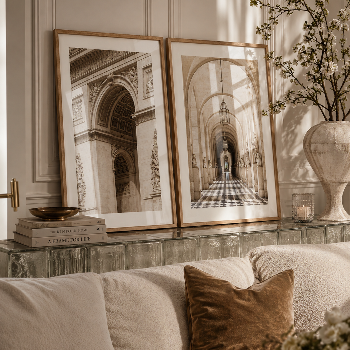 Two framed black and white architectural art prints leaning against a paneled wall above a sofa in a styled living room setting.