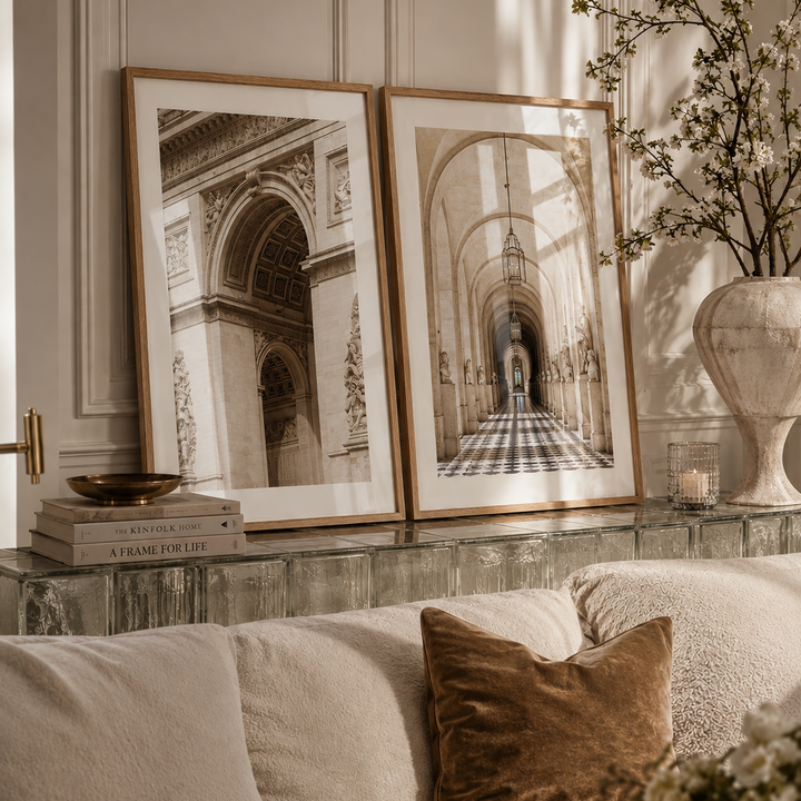 Two framed black and white architectural art prints leaning against a paneled wall above a sofa in a styled living room setting.