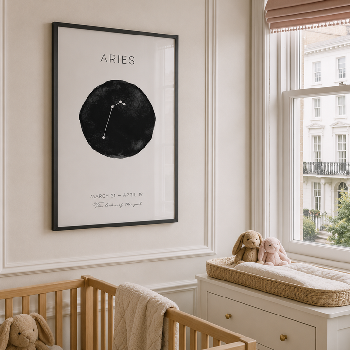 A framed Aries zodiac art print hangs on a cream-colored nursery wall above a wooden crib, with a window, changing bench, and stuffed bunny toys nearby.