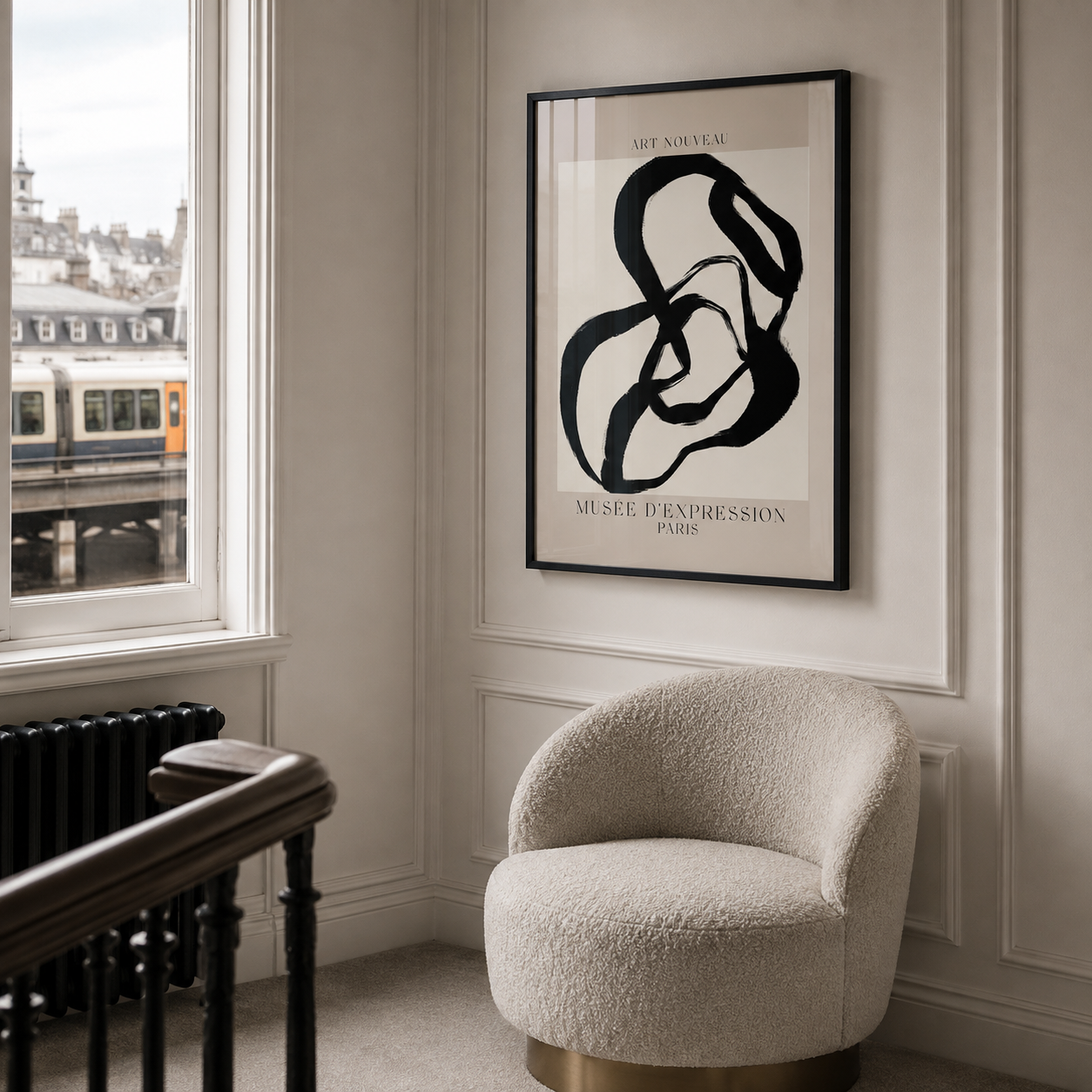 A framed abstract black and white art print hangs on a cream paneled wall in a modern interior setting with a textured cream bouclé armchair and a window showing a train outside.