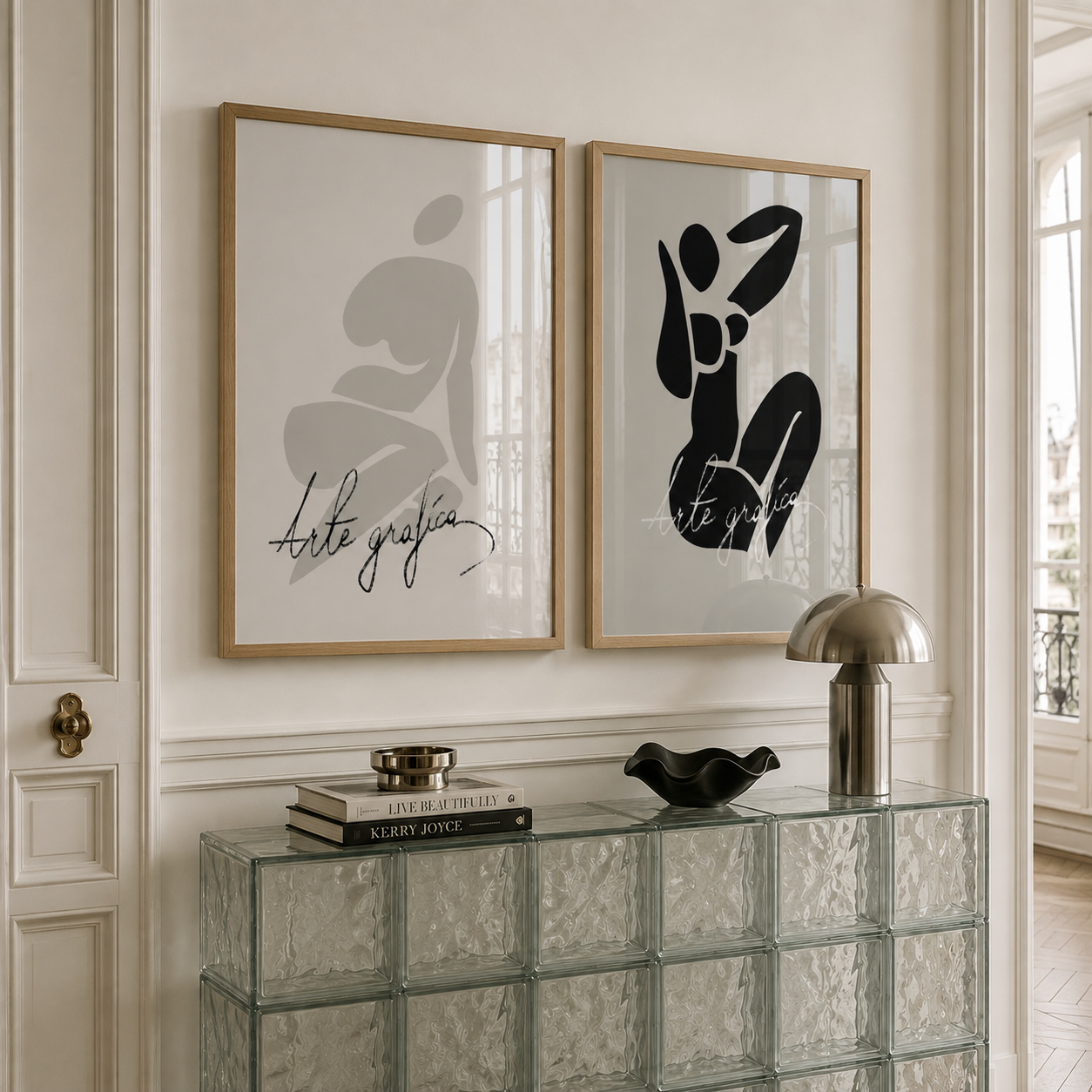 Two framed abstract art prints hang on a cream-colored wall above a glass block console table. The left print features a light gray abstract figure with the text 'arte grafica', and the right print features a black abstract figure with the text 'arte pura'.