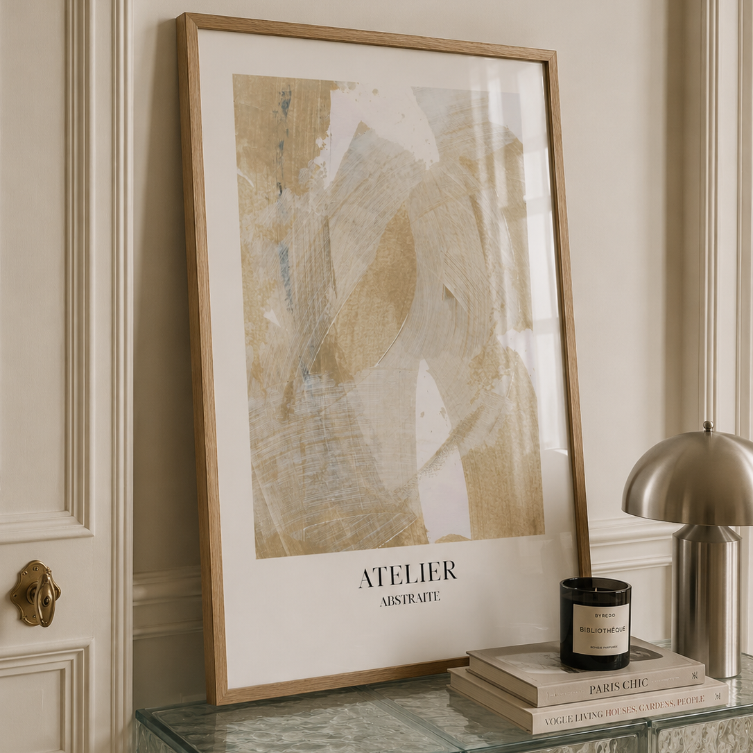 A framed abstract art print with a light wood frame and white mat, leaning on a glass-topped console table in a styled interior setting.