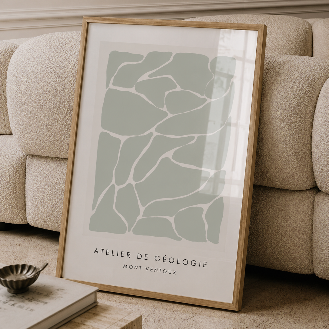 A framed art print with a minimalist geology pattern in sage green and white, styled leaning against a beige boucle sofa in a modern living room setting.
