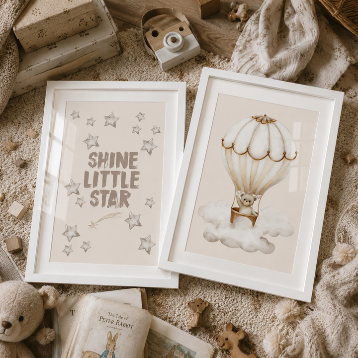 Two framed children's art prints displayed on a cozy knitted blanket with nursery props. The left print says 'SHINE LITTLE STAR' with gray stars and a small shooting star.