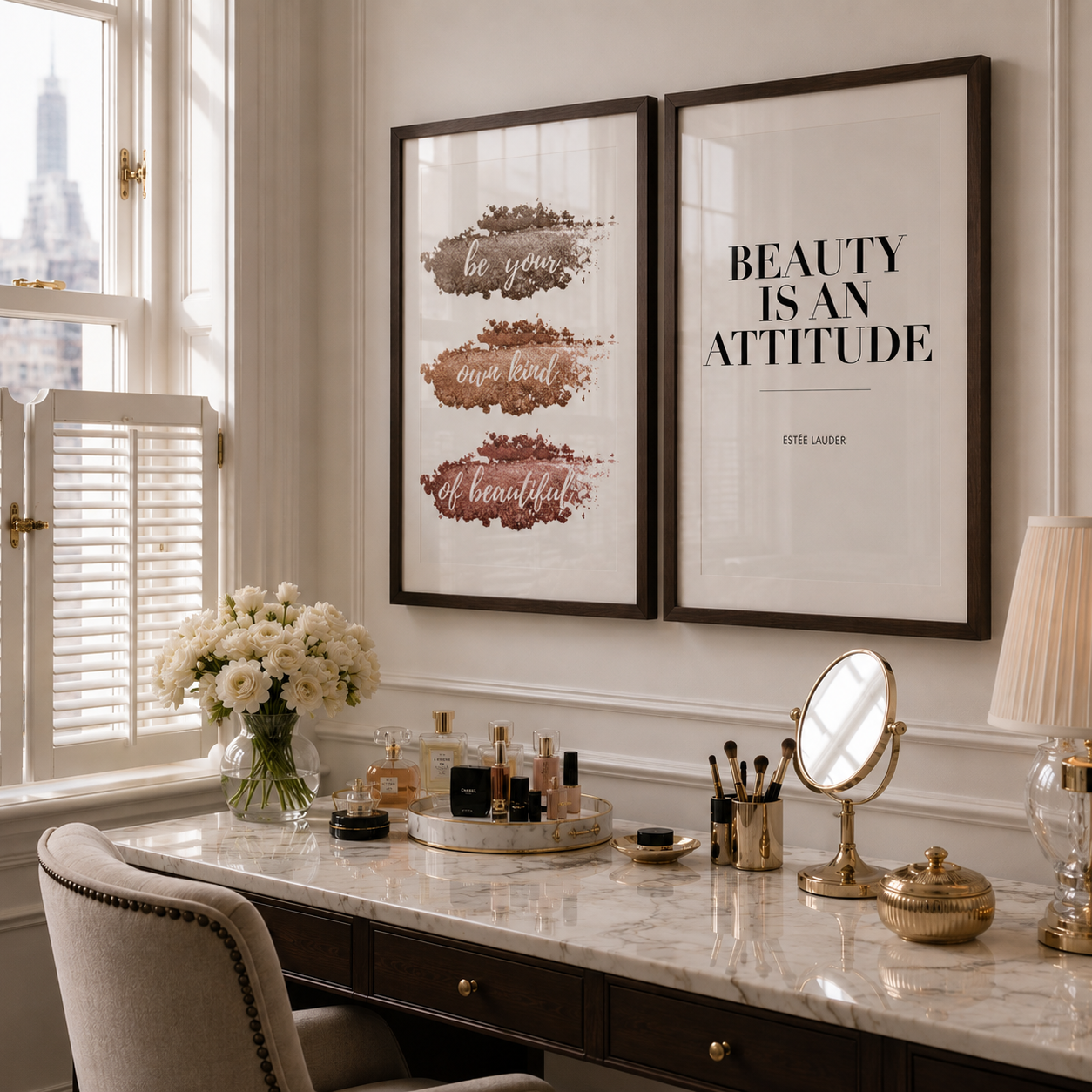 Two framed wall art prints hang above a vanity desk in a bright room. The left print has three horizontal watercolor-style brown and rose brushstrokes with decorative text, and the right print reads 'BEAUTY IS AN ATTITUDE' with a small quote below.