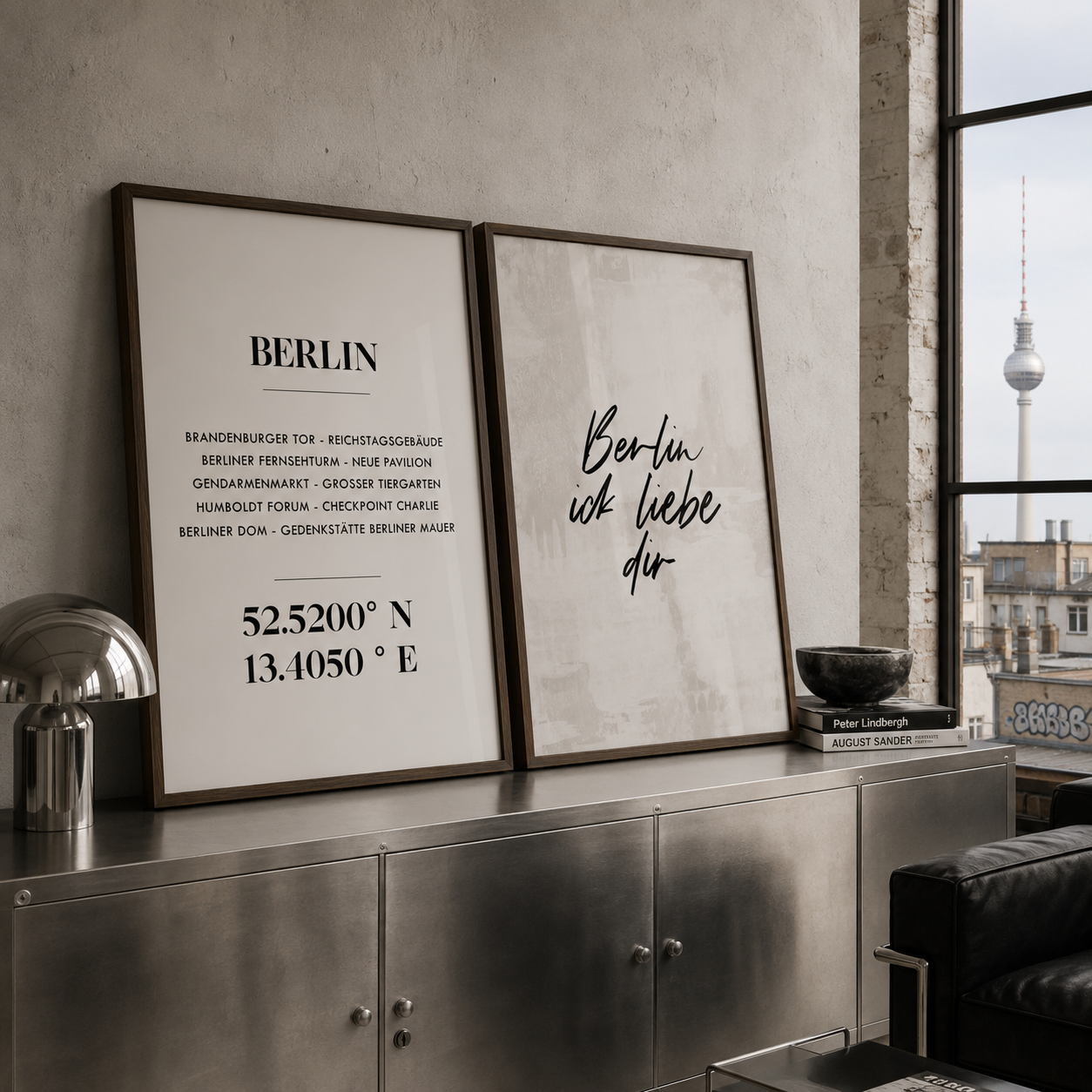 Two framed Berlin-themed wall art prints displayed on a metallic console table in a modern interior. One print features black text with coordinates and place names under the word BERLIN, and the other has black script text reading 'Berlin, ich liebe dich'.