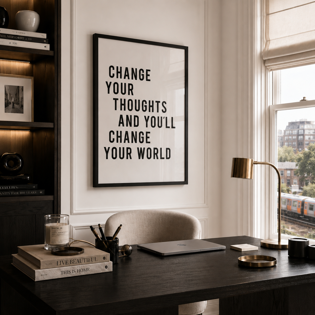 A framed typographic wall art print with the quote 'CHANGE YOUR THOUGHTS AND YOU'LL CHANGE YOUR WORLD' hangs on a white wall above a dark wood desk in a styled home office setting.