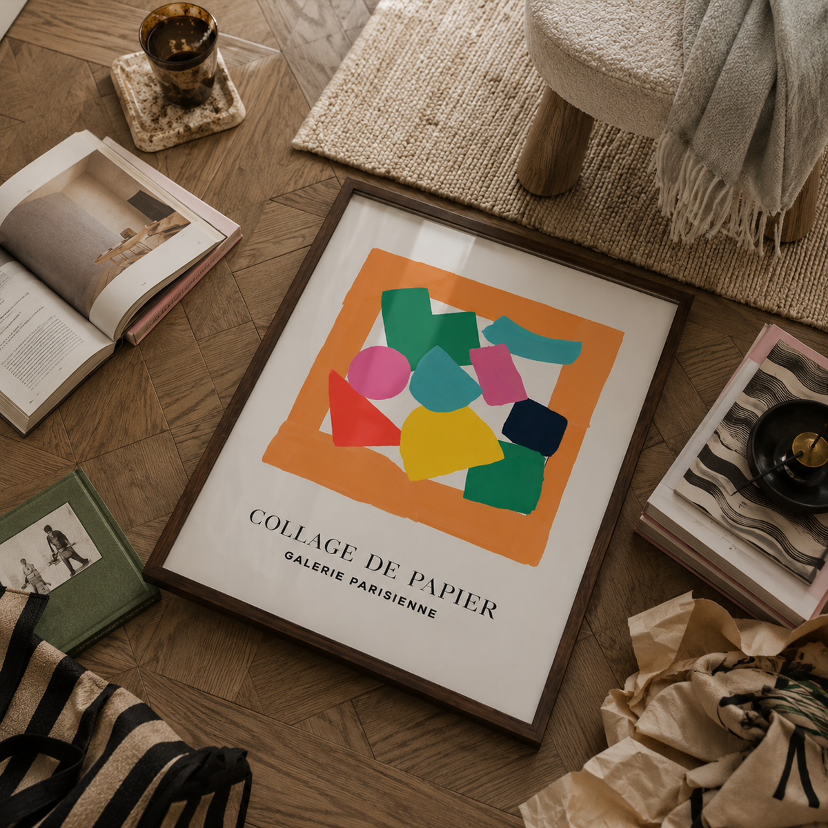A framed abstract collage art print with colorful geometric shapes on an orange square background, displayed on a wooden floor among books, a throw blanket, and other home decor items. The print includes the text 'COLLAGE DE PAPIER GALERIE PARISRIEUNE'.