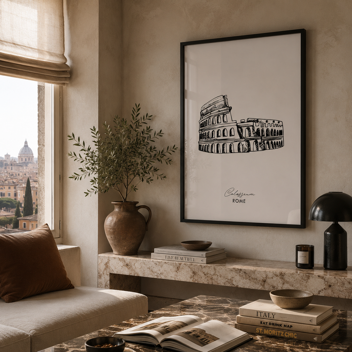 A framed black-and-white architectural art print of the Colosseum in Rome hangs on a beige wall in a styled living room setting with a marble console table, books, a lamp, and a window view.