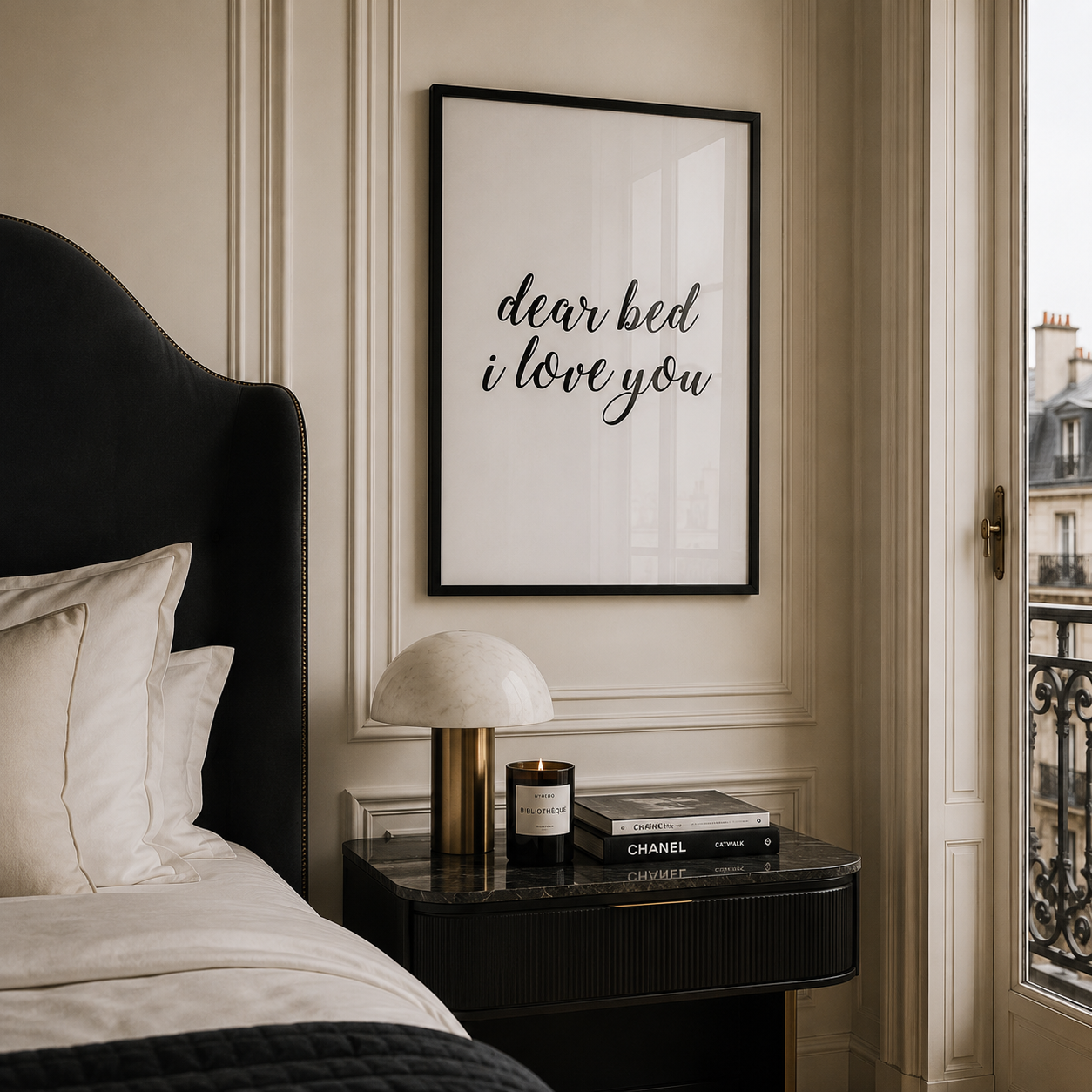 Bedroom with a black upholstered headboard, nightstand with a candle and book, and framed artwork on the wall.