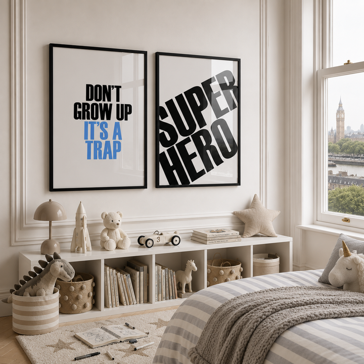 Two framed wall art prints displayed above a white shelf in a styled children's bedroom. The left print reads 'DON'T GROW UP IT'S A TRAP' in black and blue text, and the right print reads 'SUPER HERO' in large black letters.