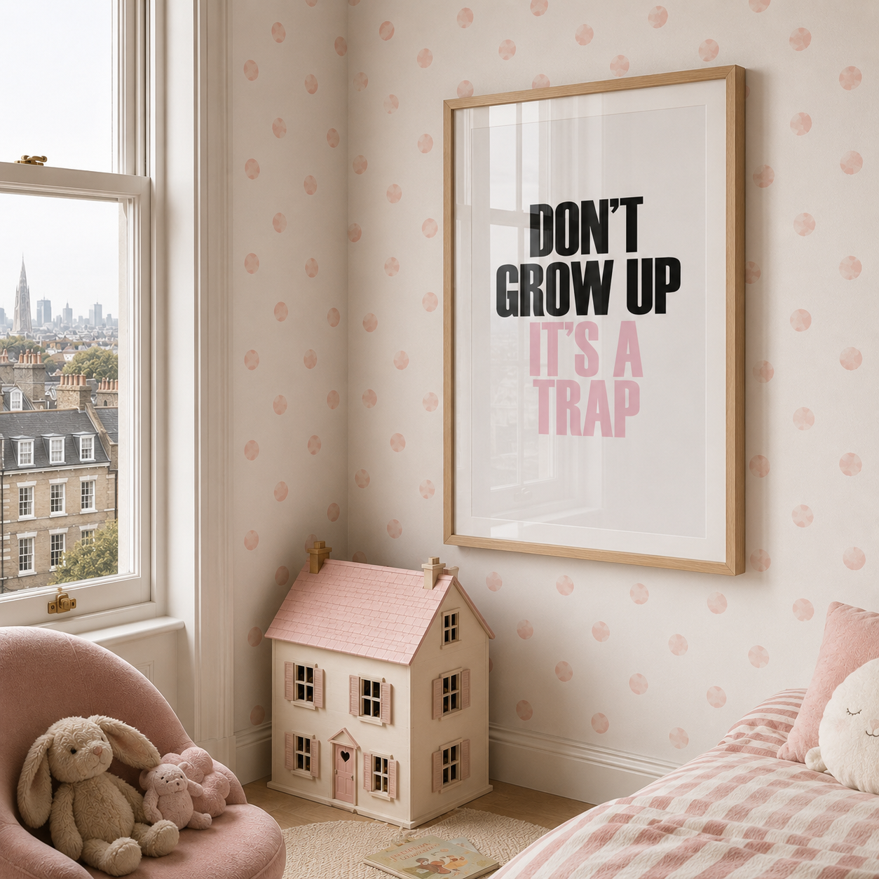 A framed wall art print with the text 'DON'T GROW UP IT'S A TRAP' in black and pink lettering, displayed in a light wood frame on a pink patterned wall in a child's bedroom. A dollhouse, pink armchair, stuffed bunny, and bed are visible in the room.
