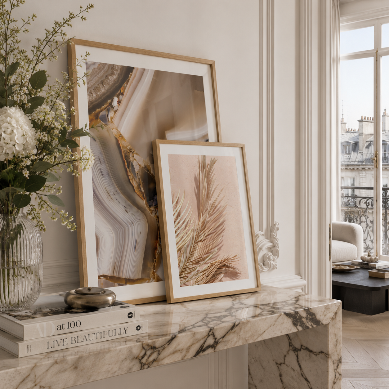 Two framed abstract botanical art prints in light wood frames, styled on a marble console table in a bright, elegant room.