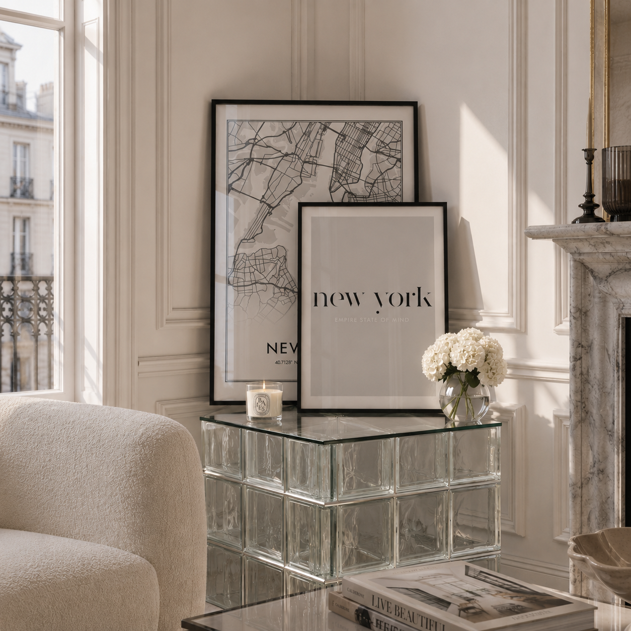 Two framed minimalist art prints with black frames are displayed on a glass block side table in a bright, elegant room. One print features a black-and-white street map of New York, and the other has the text 'new york' in black.
