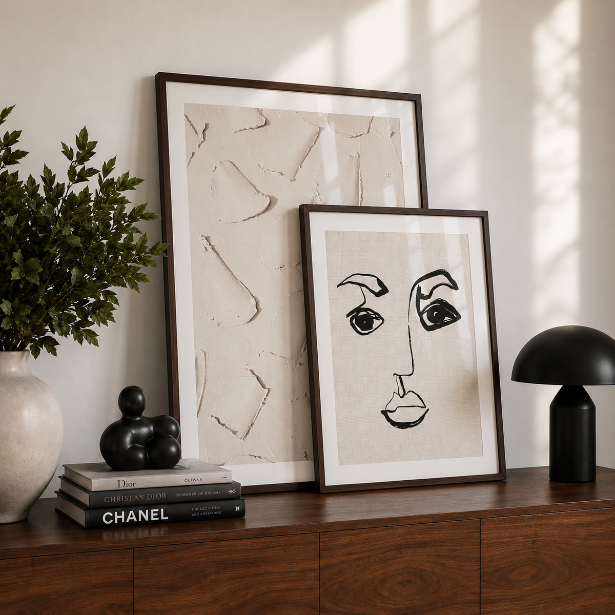 Two framed artworks on a wooden surface with a lamp and books in the background.