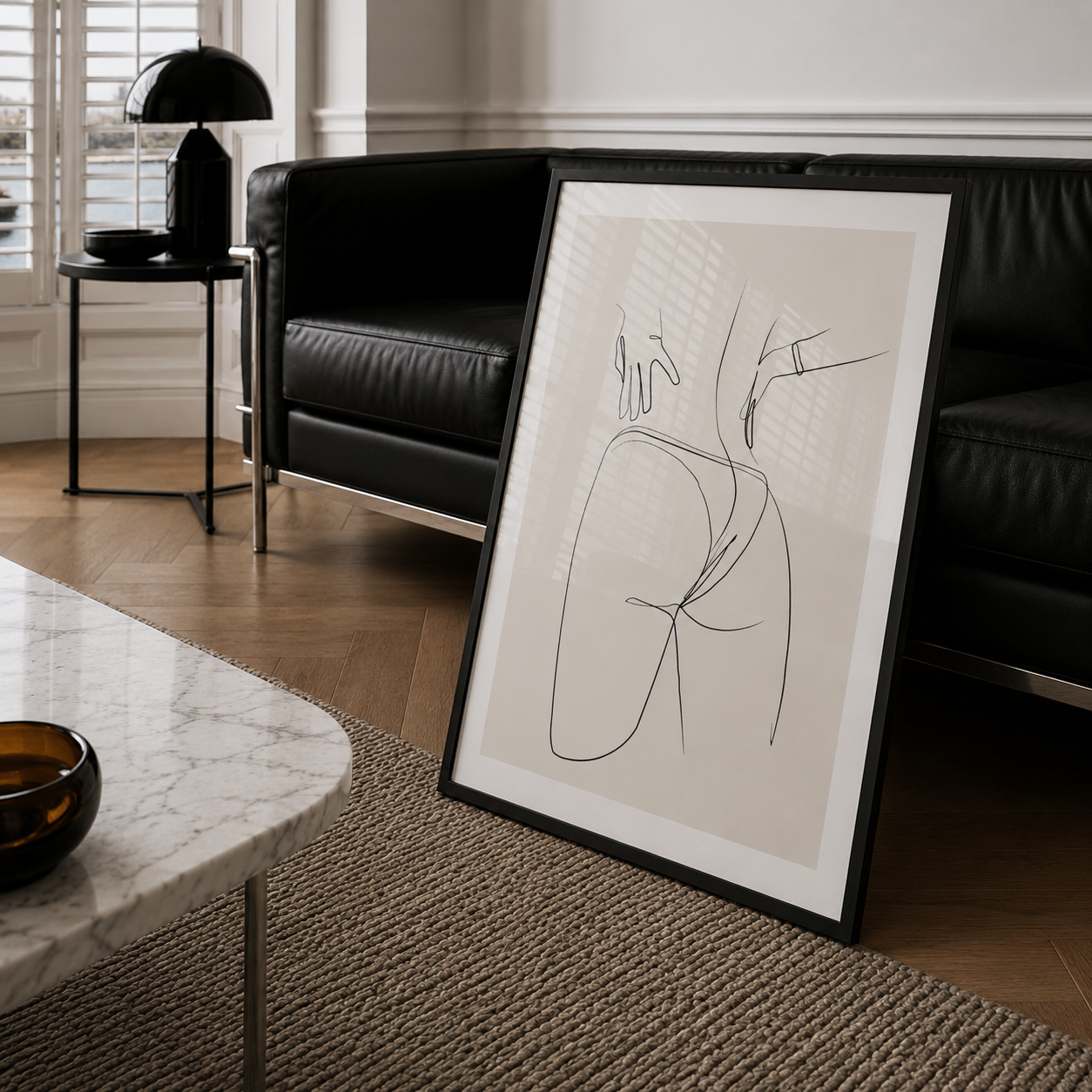 Framed abstract line art in a modern living room with a black sofa and marble table.