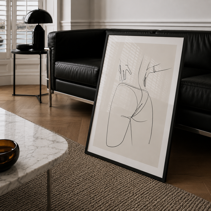 Framed abstract line art in a modern living room with a black sofa and marble table.