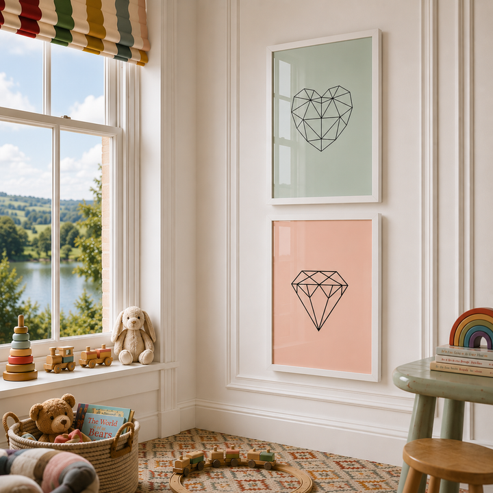 A styled children's room corner with two framed wall prints hanging above a rug. The prints show a geometric heart on a pale green background and a geometric diamond on a pale pink background, both in white frames.