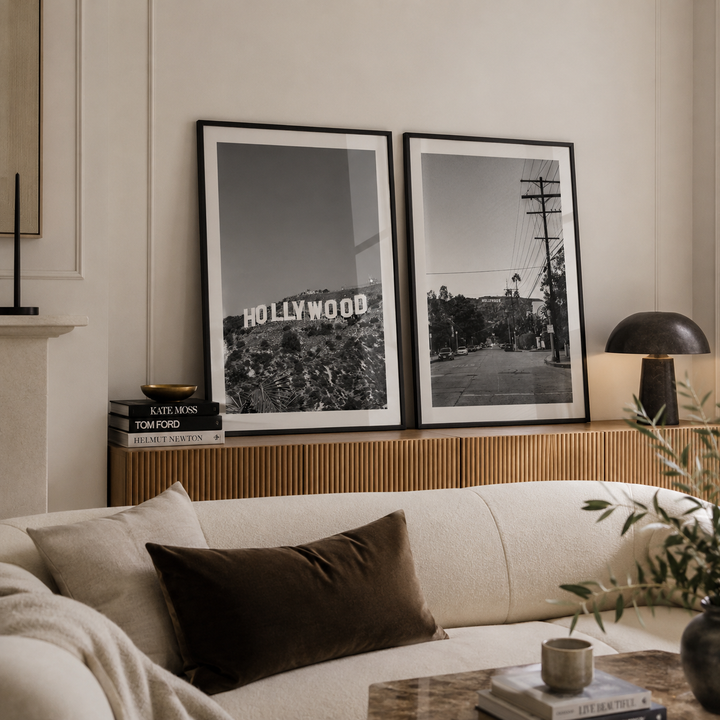 Two framed black and white art prints of the Hollywood sign and a street scene, displayed on a wooden console above a cream sofa in a modern living room setting.