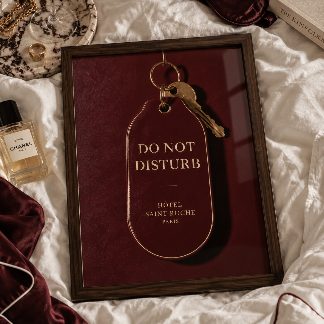 A dark burgundy hotel key tag with gold lettering reading 'DO NOT DISTURB' and 'HÔTEL SAINT ROCHE PARIS', attached to a gold key ring with a brass key, shown against a matching burgundy background.