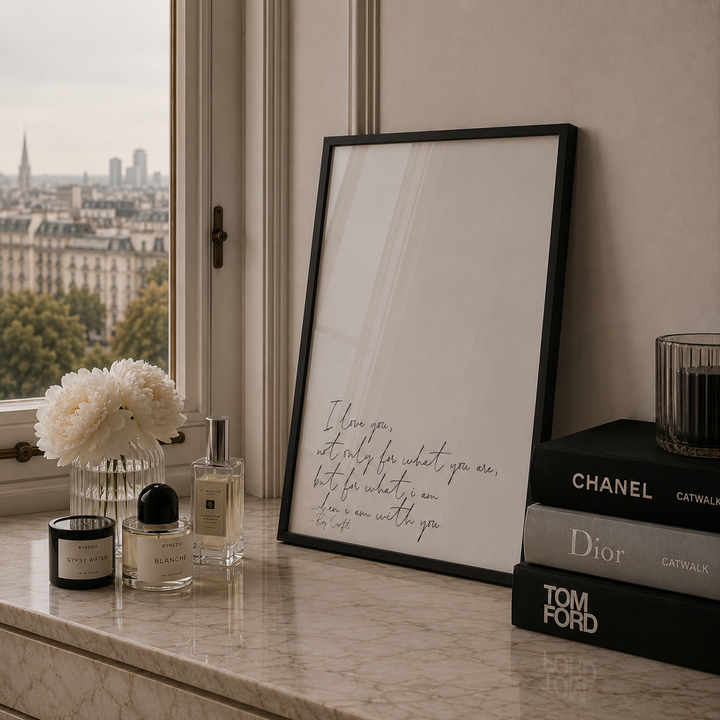 Framed artwork on a marble surface with candles, flowers, and books.