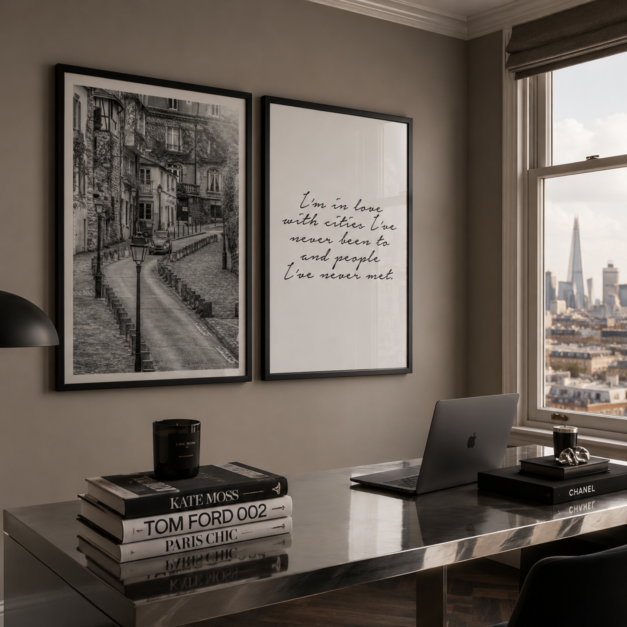 Two framed black-and-white wall art prints hang on a taupe wall above a reflective desk in a modern room. The left print shows a Montmarte street scene, and the right print features cursive text reading, 'I'm in love with cities.