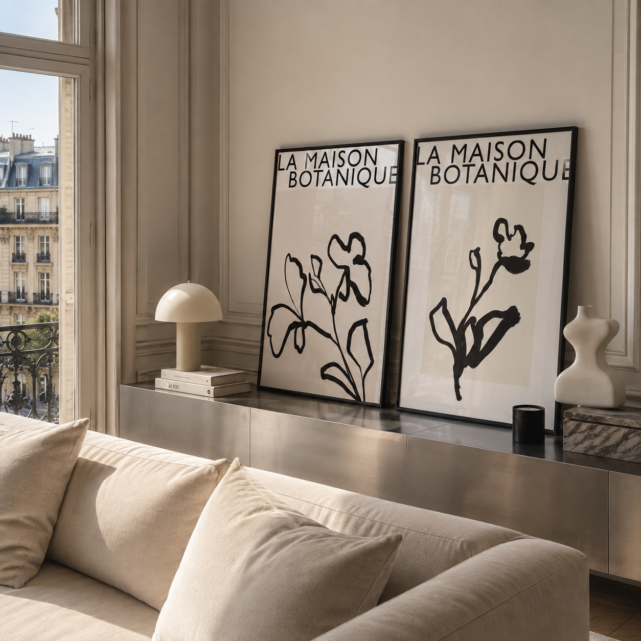 Two framed botanical art prints with black line drawings and the text 'LA MAISON BOTANIQUE' hang on a beige wall above a console table in a modern living room setting.