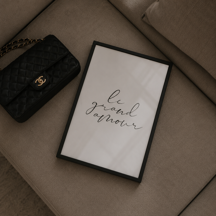 Framed artwork with 'le grand amour' text on a beige surface next to a black handbag.