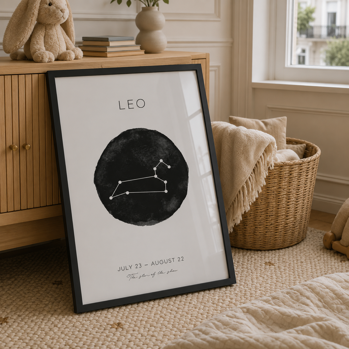A framed art print featuring a black watercolor circle with a Leo constellation design and the text 'LEO' and 'JULY 23 - AUGUST 22' leans against a wooden cabinet in a cozy, sunlit room with a woven basket and beige textiles.