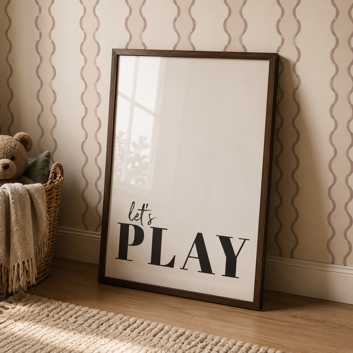 A framed typographic wall art print leaning against a patterned wallpaper wall on a wooden floor. The print has a dark brown wood frame, a white background, and the text 'let's PLAY' in black.
