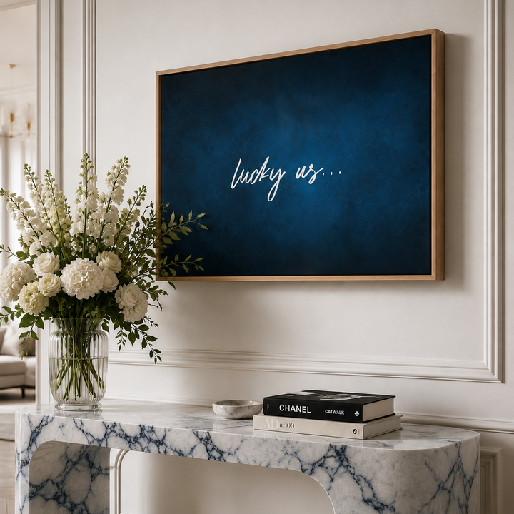 A large framed canvas wall art print with a dark blue textured background and white script text reading 'lucky us.