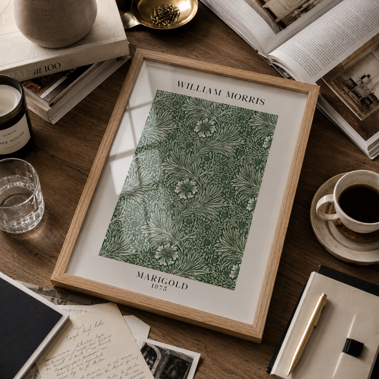 A framed William Morris Marigold 1935 art print featuring a green and white floral pattern, styled on a wooden desk with books, a coffee cup, and stationery.