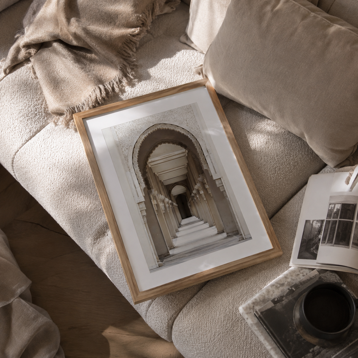 A framed black and white architectural photograph of a grand archway and staircase, presented in a light wood frame on a textured beige sofa with a throw blanket and pillows.