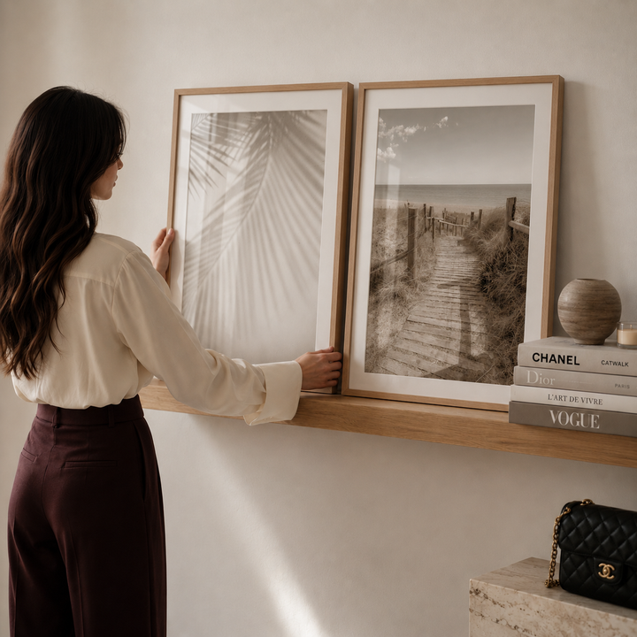 Woman arranging framed pictures on a wall shelf with decor items below.