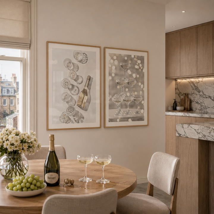 Dining room with a table set for a meal, including a bottle of champagne, glasses, and grapes. Two framed artworks on the wall.
