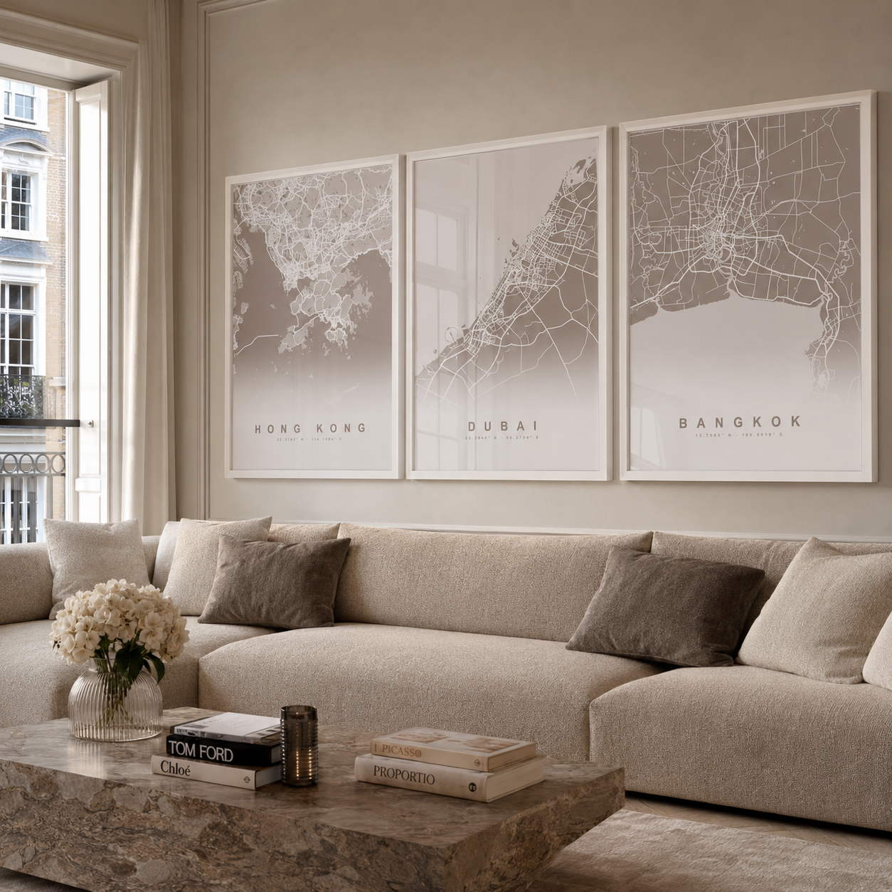 Three framed minimalist city map prints labeled Hong Kong, Dubai, and Bangkok hang above a beige sectional sofa in a softly styled living room.