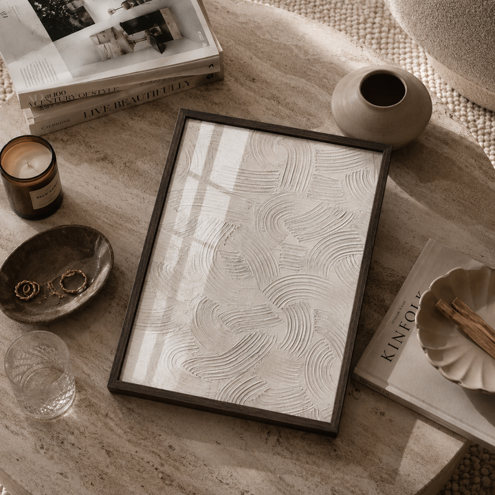 Framed artwork on a textured surface with books, a candle, and a vase.
