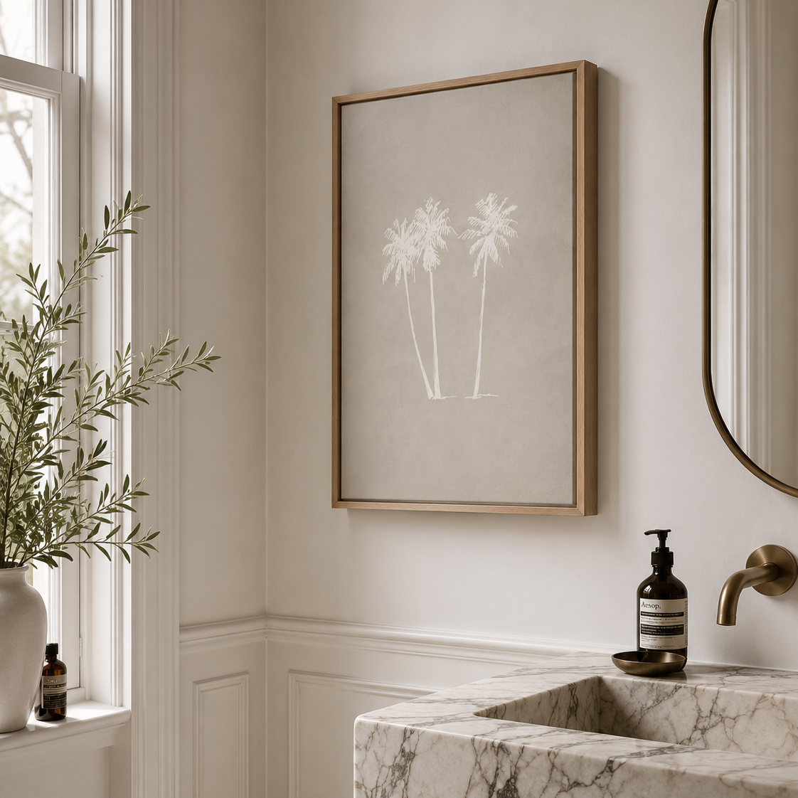 A large framed stretched canvas wall art print featuring soft white palm tree silhouettes on a warm beige background, hanging in a luxury styled bathroom corner above a marble sink with a gold faucet.