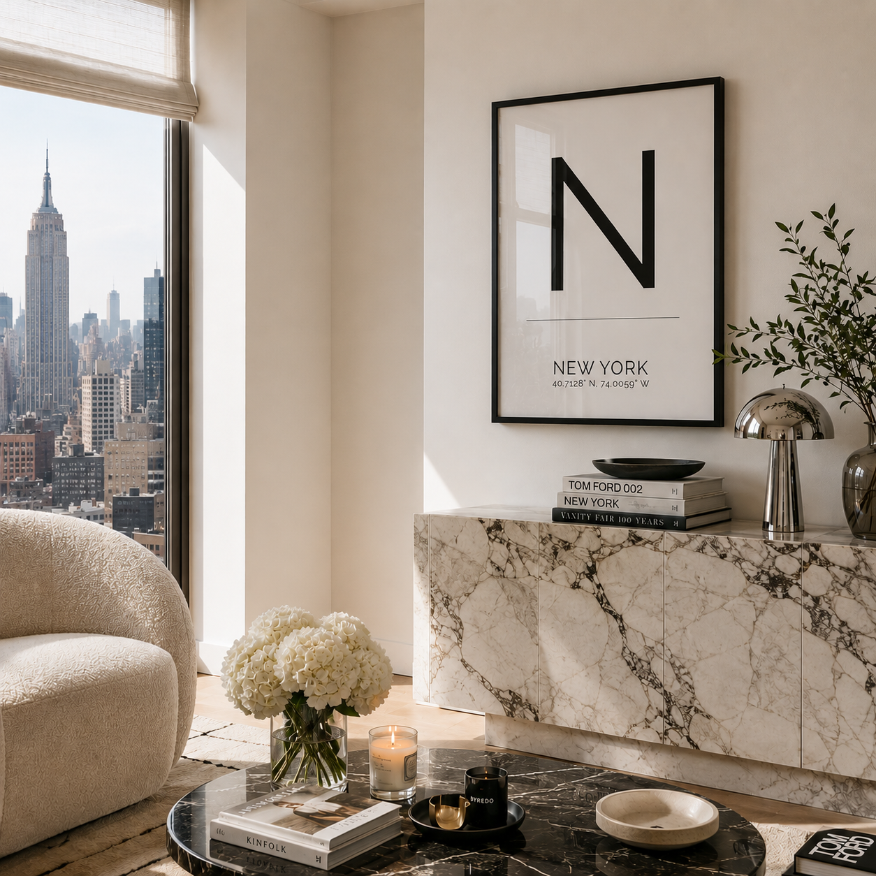 A framed black-and-white art print featuring a large letter N and the text 'NEW YORK' hangs on a cream wall above a marble console. The room is styled with a beige armchair, a black marble coffee table, white flowers, books, and a silver lamp, with a city skyline visible in the background window.