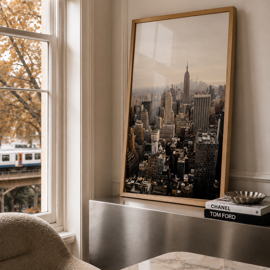 A large framed art print of a New York City skyline leaning against a wall on a marble-topped desk in a modern office setting.