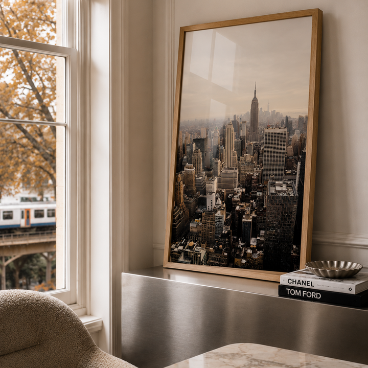 A large framed art print of a New York City skyline leaning against a wall on a marble-topped desk in a modern office setting.