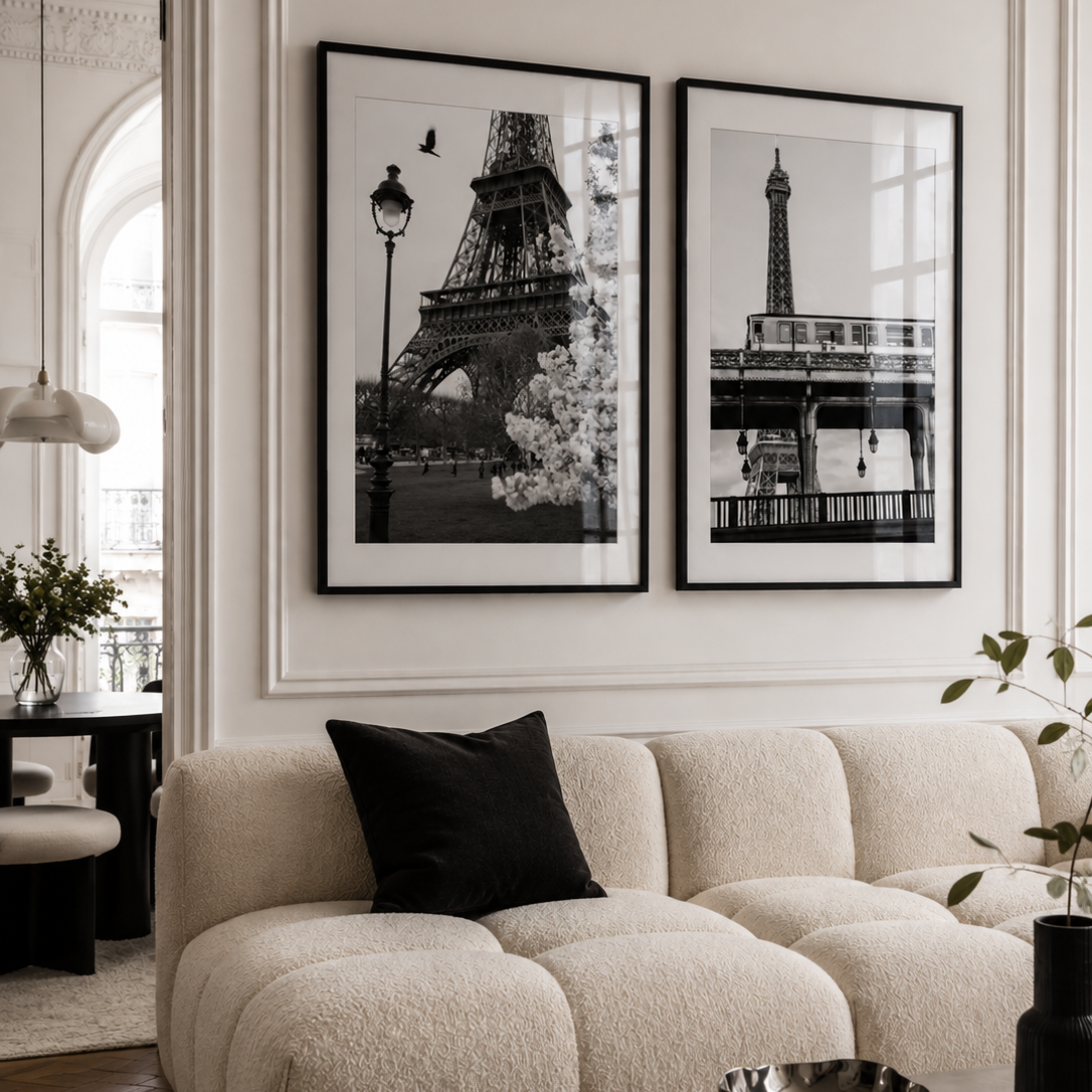 A styled living room featuring two black and white framed art prints of the Eiffel Tower hanging on a cream-colored wall above a beige boucle sofa with a black accent pillow.