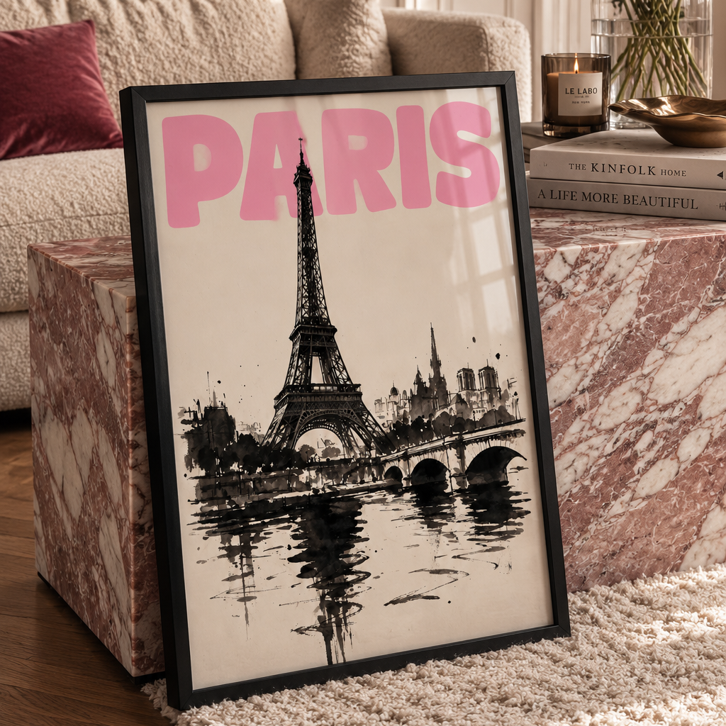 A framed black and white Paris cityscape print with bold pink 'PARIS' lettering, leaning on a marble side table in a styled living room with flowers and a sofa in the background.