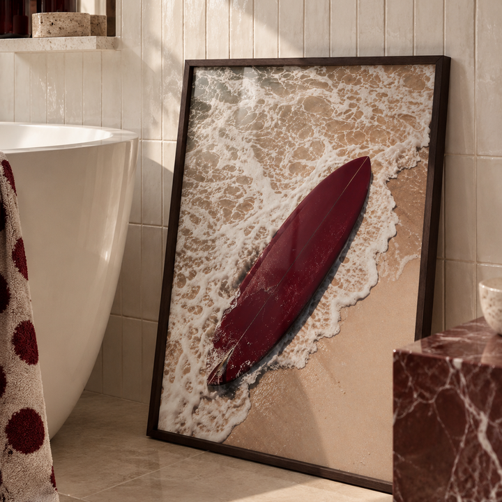 a photo of a deep red surfboard on the beach in a dark wood frame in a luxury bathroom.
