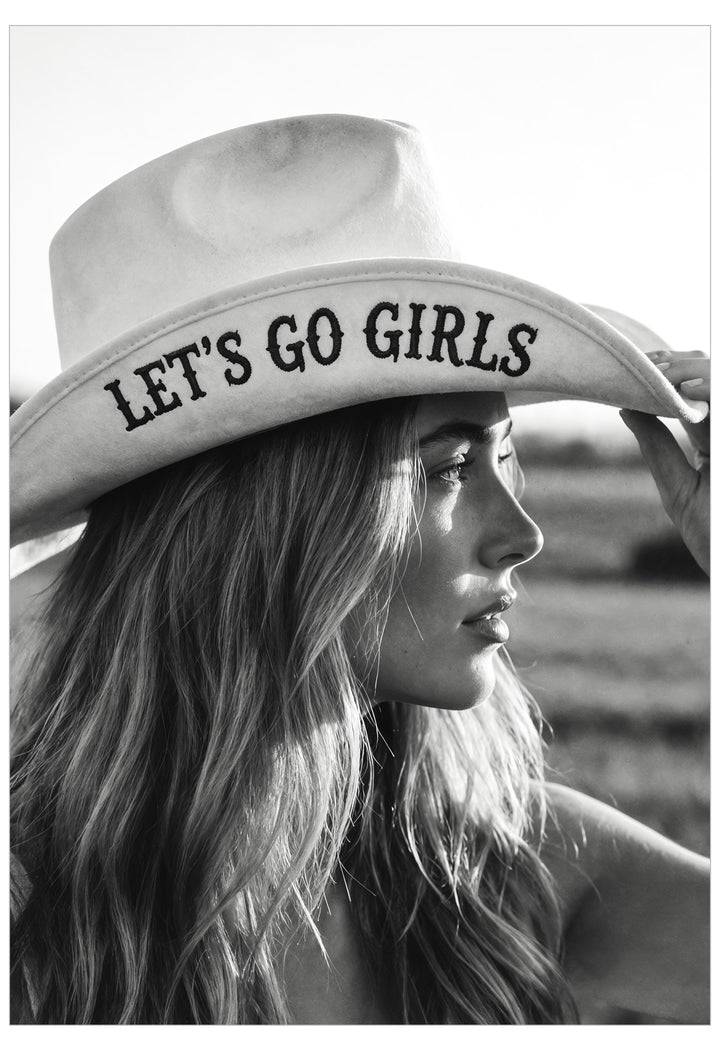 A black and white lifestyle photograph of a woman in profile wearing a cowboy hat with the text 'LET'S GO GIRLS' printed on the brim.