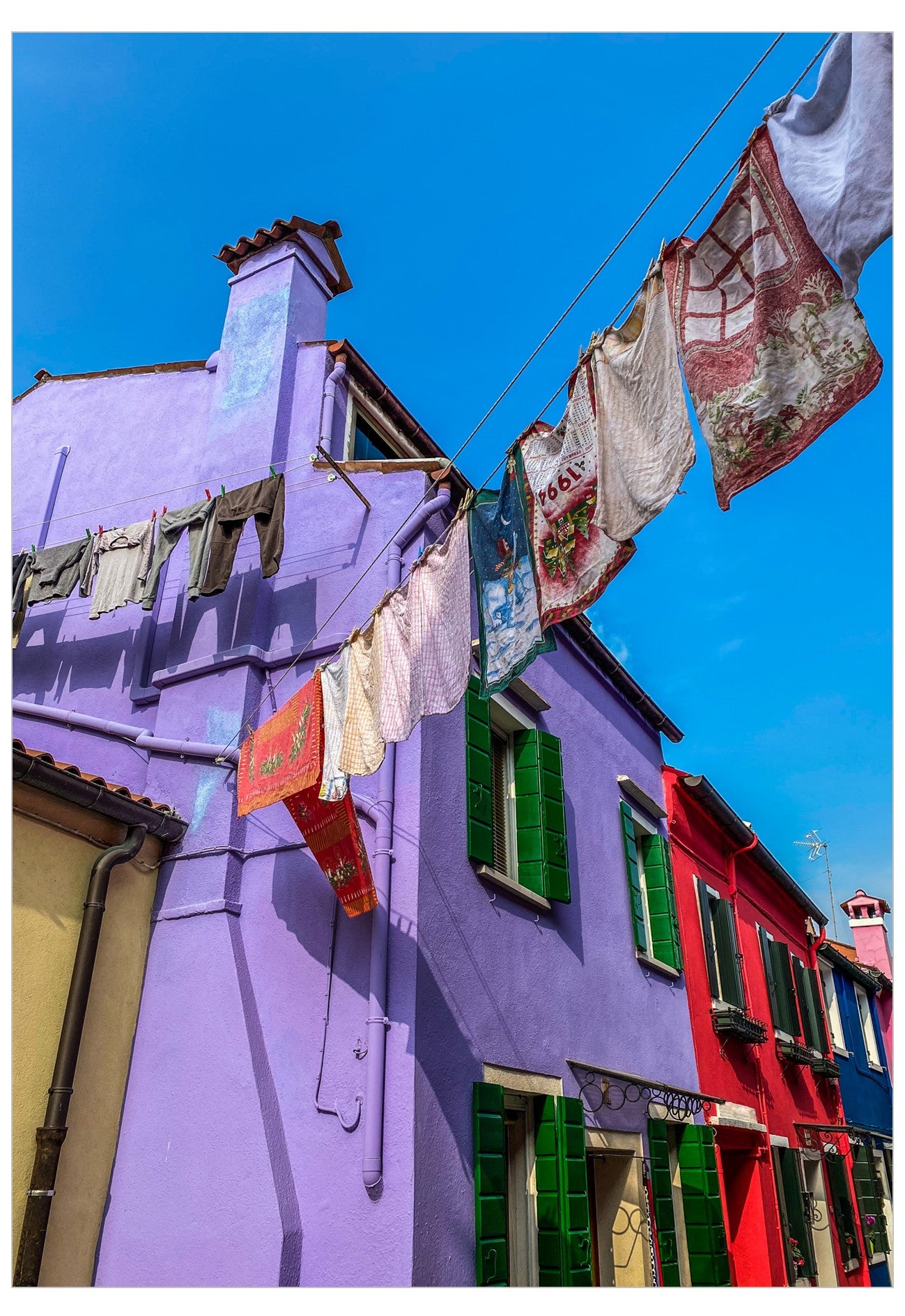 Colorful Italian-style buildings under a bright blue sky, with laundry hanging on clotheslines across the scene.