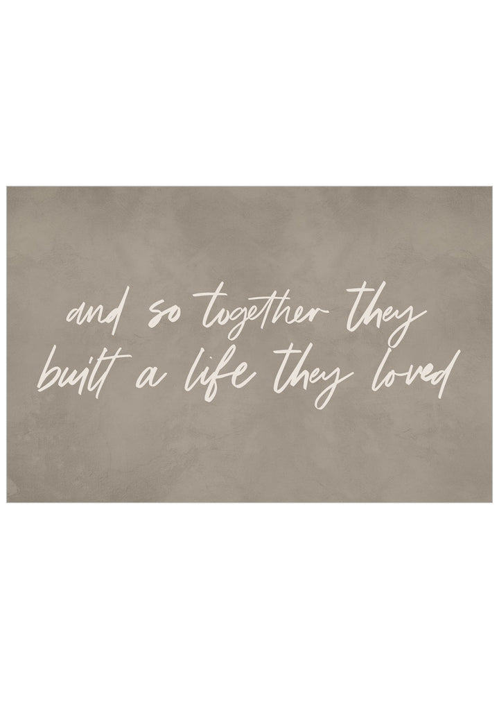 A rectangular wall art print with a textured taupe-brown background and white script text reading, 'and so together they built a life they loved.'.