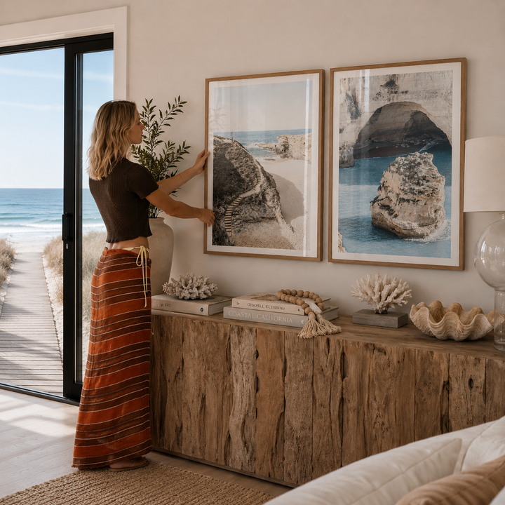 Woman arranging decor in a room with beach-themed artwork and natural elements.