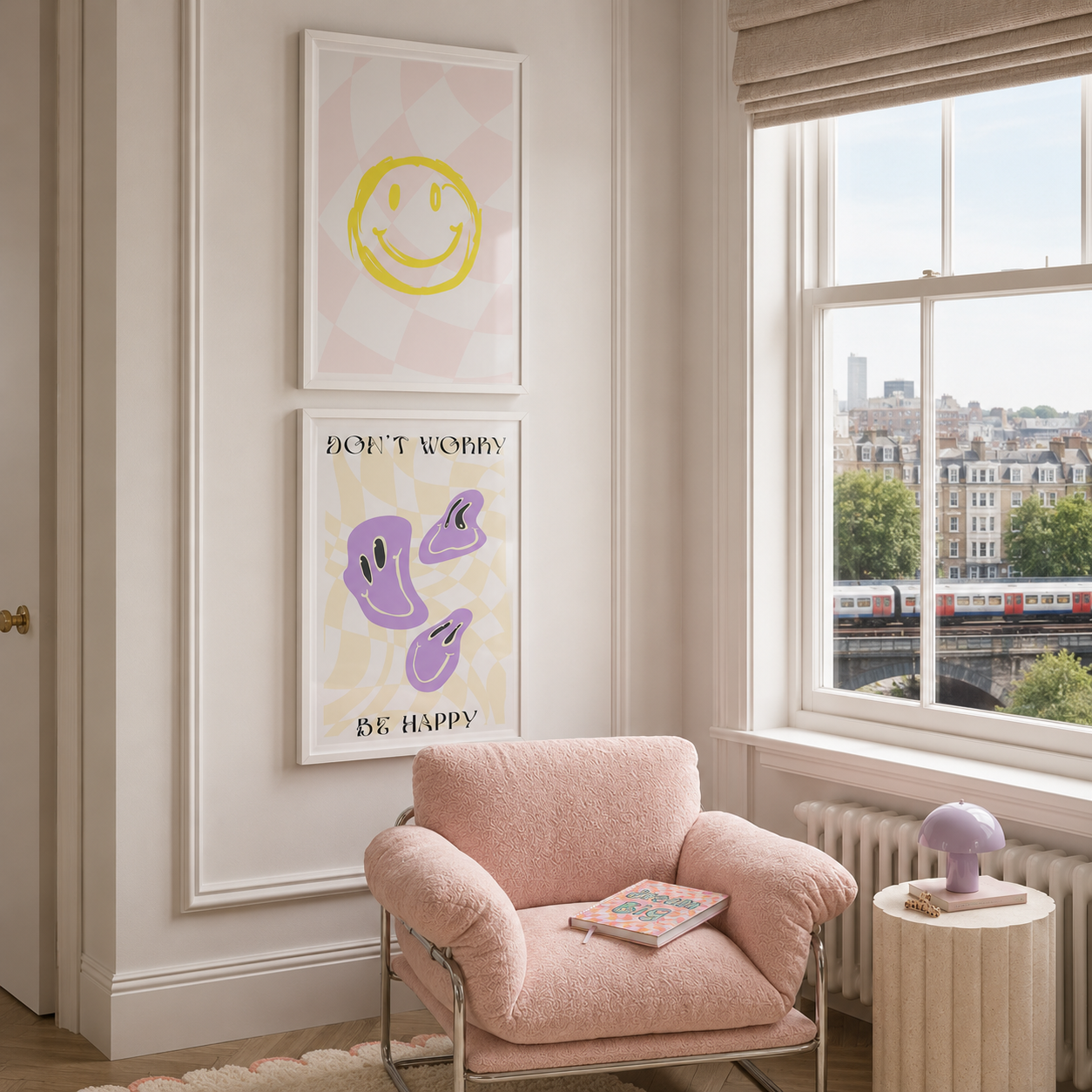 A styled interior room with a pink armchair, a small side table, and two framed wall art prints hanging above the chair. The lower print reads “DON’T WORRY BE HAPPY” with purple abstract shapes on a pale yellow background.