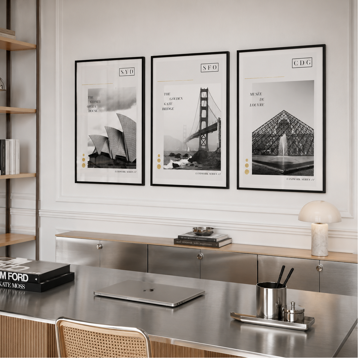 Three framed black-and-white architectural art prints hang on a white wall above a modern desk in a styled interior room. The prints feature the Sydney Opera House, Golden Gate Bridge, and Louvre Pyramid with stylized city labels.